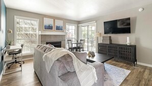 A modern living room with a gray sectional sofa, a fireplace, a dining area, and a TV mounted on the wall. - Landing | Beautiful 1BD, Pool, Clubhouse (San Antonio)