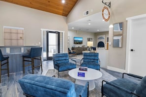 A spacious lobby with a reception desk, several seating areas with blue chairs, a round coffee table, and a large window offering a view of the outdoors.