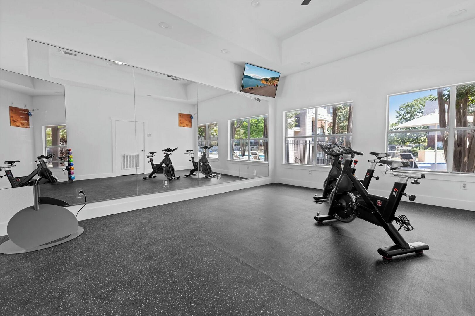 Una palestra con cyclette, ampie finestre e un televisore appeso al muro.
