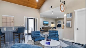 A spacious lobby with a reception desk, several seating areas with blue chairs, a round coffee table, and a large window offering a view of the outdoors.