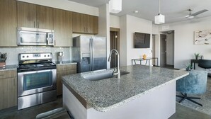 Een moderne keuken met roestvrijstalen apparatuur, een eiland met een granieten werkblad en een eethoek met een kleine tafel en stoelen.