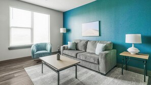 Un salon moderne avec un canapé gris, un fauteuil bleu, une table basse et deux lampes posées sur des tables d’appoint.