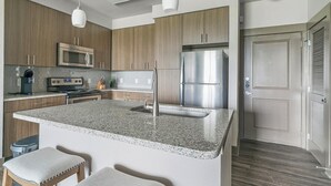 A modern kitchen with granite countertops, stainless steel appliances, and wooden cabinetry. - Landing | Stylish 1BD, Gym (Houston)