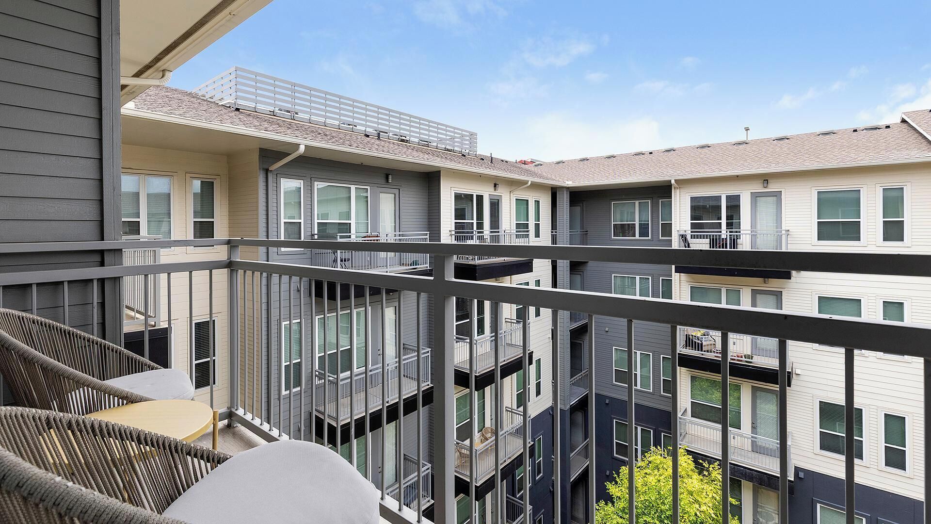 Un edificio residencial de varios pisos con balcones, un área de estar al aire libre techada y un cielo despejado.