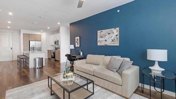 Una sala de estar moderna con un sofá color beige, una mesa de centro de cristal y una pared de acento azul.