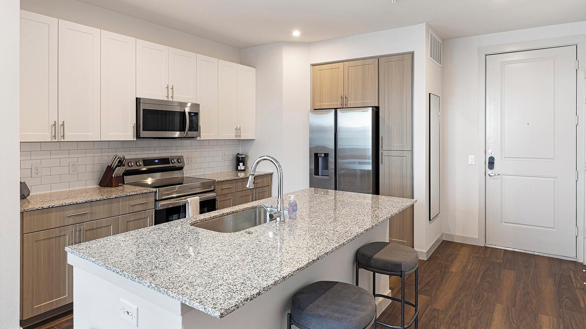 A modern kitchen with white cabinets, stainless steel appliances, granite countertops, and a built-in oven.