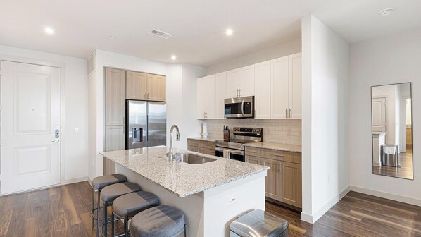 A modern kitchen with white cabinets, stainless steel appliances, and a granite countertop.