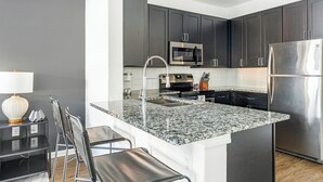 A modern kitchen with dark cabinets, stainless steel appliances, a granite countertop, and a bar stool. - Landing | Beautiful 1BD, Pool, Gym (Austin)