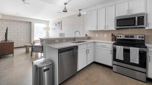 A modern kitchen with stainless steel appliances, white cabinetry, and a tiled backsplash.