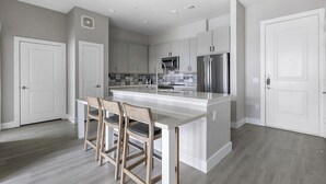 Cozinha moderna com ilha central, banquetas e eletrodomésticos de aço inoxidável.