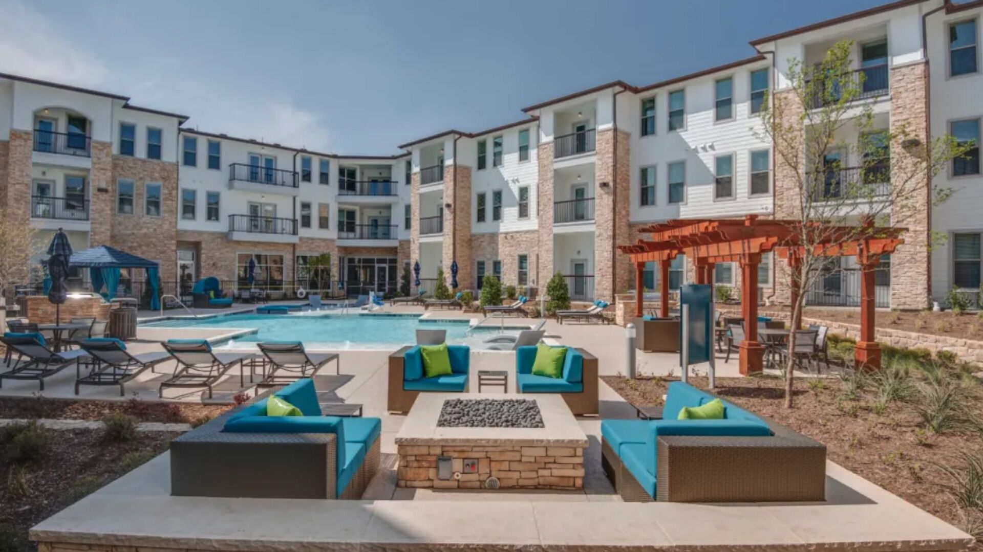 A poolside area with lounge chairs and a fire pit, surrounded by multi-story buildings with balconies.