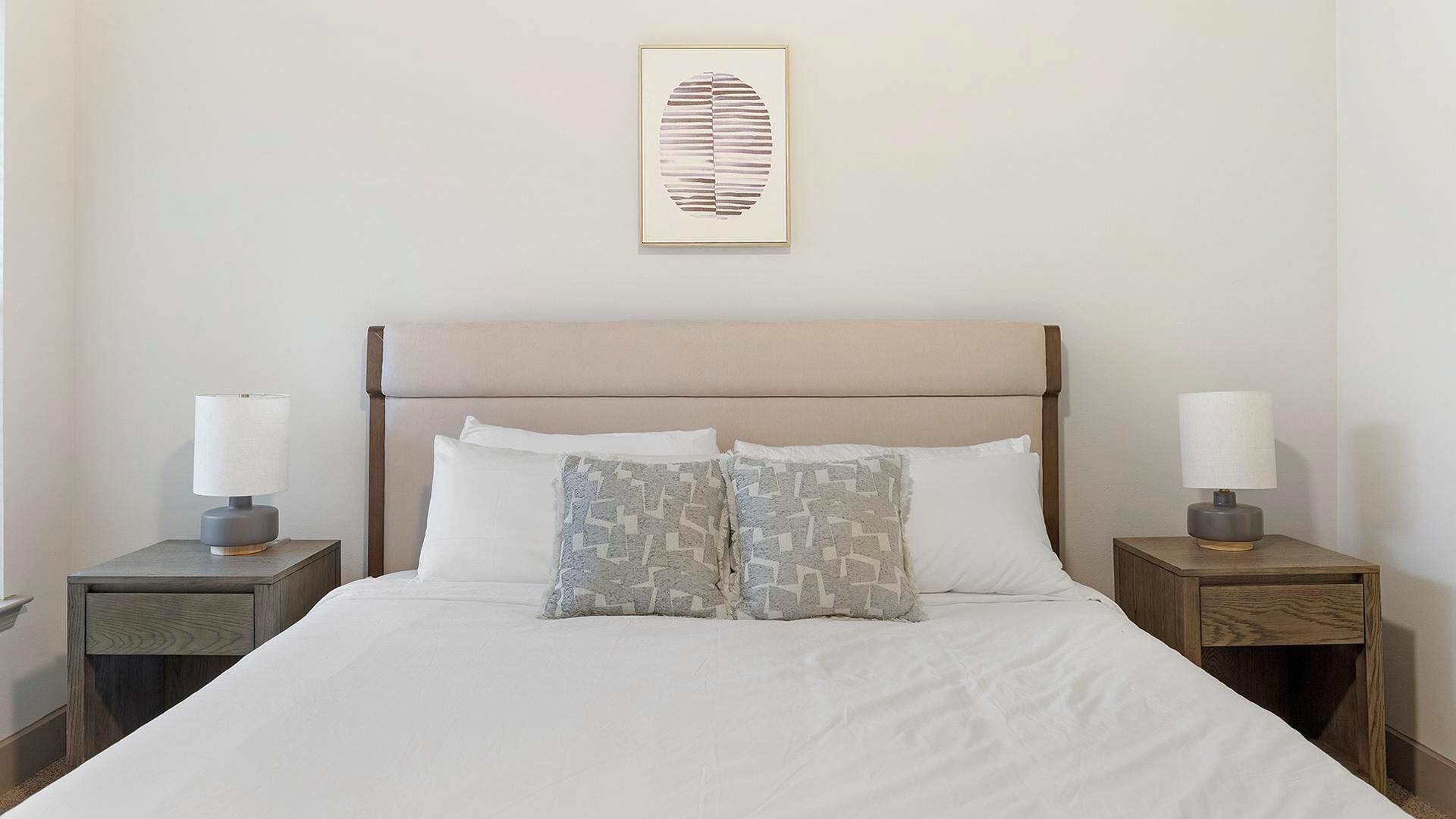 A neatly made bed with white linens, two bedside tables with lamps, and a framed artwork above the bed.