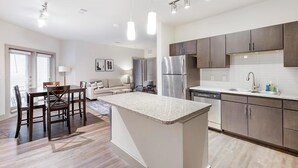 A modern kitchen with dark cabinets, a stainless steel refrigerator, and a granite countertop island. - Landing | Amazing 2BD, Courtyard, Clubhouse (Haltom City)