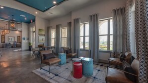 A spacious living room with a high ceiling, large windows, and a view of the outdoors. There are several seating areas with leather chairs and a coffee table. - Landing | Amazing 2BD, Courtyard, Clubhouse (Haltom City)