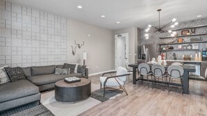 Un salon moderne avec un canapé d’angle gris, une table basse ronde et un coin repas comprenant une table sombre et des chaises grises.