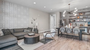 A modern living room with a gray sectional sofa, a round coffee table, and a dining area with a dark table and gray chairs.