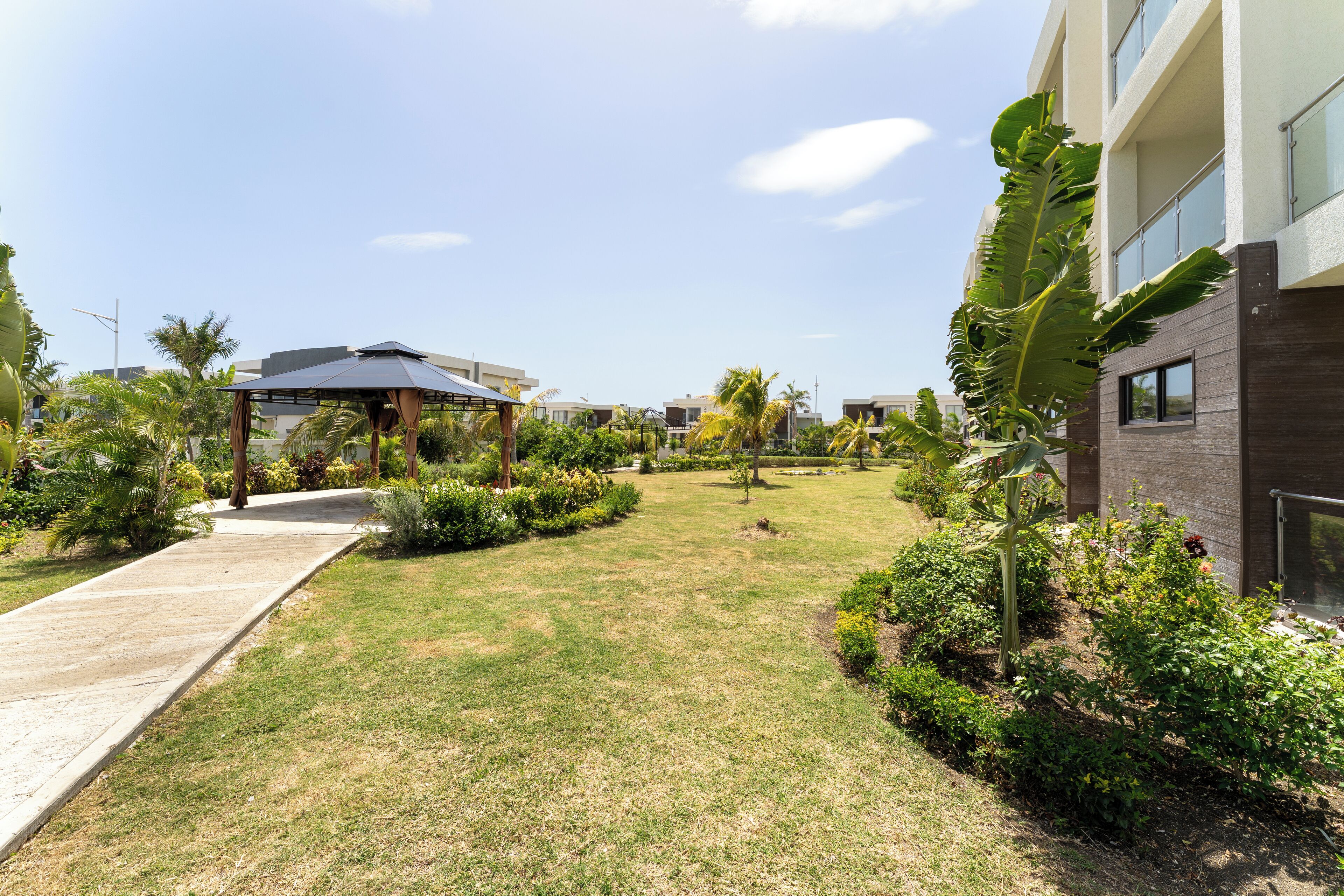 A modern hotel courtyard with a paved walkway, lush greenery, and a covered seating area.