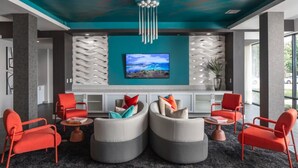 Un hall d’entrée moderne agrémenté d’un mur d’accent de couleur turquoise, d’un grand téléviseur à écran plat et d’un espace salon avec des fauteuils et des poufs rouges et gris.