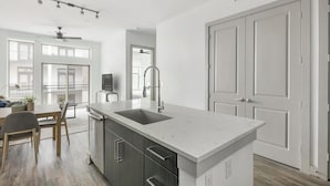 Une cuisine moderne dotée d’un îlot central, de meubles de rangement aux couleurs sombres et d’une grande fenêtre.