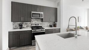 Une cuisine moderne avec des meubles de couleur sombre, un four à micro-ondes en acier inoxydable, une cuisinière à gaz et un plan de travail en marbre blanc.