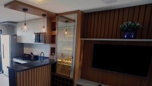 A modern kitchen with a built-in microwave, stove, and wooden cabinetry. There is a glass-fronted wine rack and a flat-screen TV mounted on the wall. - Luxury Apartment with Sea View (Matinhos)