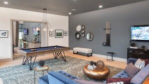 A modern living room with a pool table, a sofa, a coffee table, and a television.