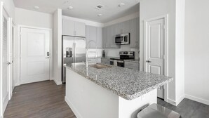 Una cocina moderna con armarios blancos, encimera de granito, electrodomésticos de acero inoxidable y microondas integrado.