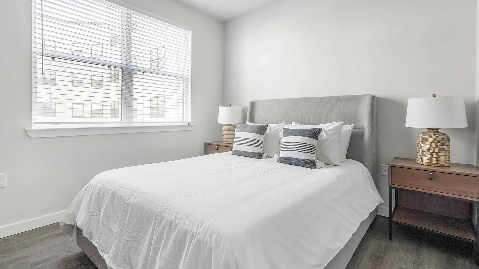 Une chambre avec un grand lit, deux tables de chevet et une fenêtre avec des stores.