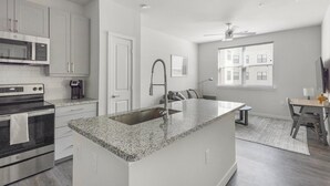 Una cocina moderna con encimeras de granito, un lavamanos integrado, electrodomésticos de acero inoxidable y un comedor con mesa y sillas.
