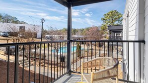 A balcony with a view of a swimming pool, a fenced patio area, and a building in the background. - Landing | Amazing 1BD, Gym, Pool (Vestavia Hills)