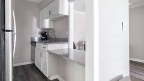A compact kitchen with white cabinets, a granite countertop, and a coffee maker. - Landing | Amazing 1BD, Gym, Pool (Vestavia Hills)