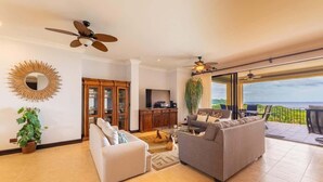 A spacious living room with a large sofa, a coffee table, and a TV. There is a balcony with a view of the ocean. - Malinche 422B- Ocean view condo at Reserva Conchal (Reserva Conchal)