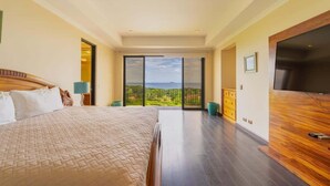 A spacious bedroom with a large bed, a flat-screen TV, and a balcony with a view of the landscape. - Malinche 422B- Ocean view condo at Reserva Conchal (Reserva Conchal)