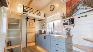 Une cuisine moderne avec un espace nuit en mezzanine, des étagères en bois et une grande fenêtre.