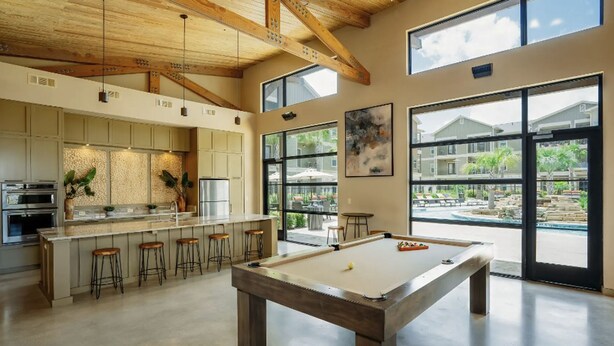 A spacious kitchen with a central island, bar stools, and a pool table in a bright room with large windows.