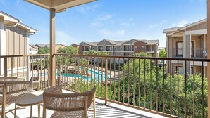 A balcony with wicker furniture overlooking a swimming pool and apartment buildings.