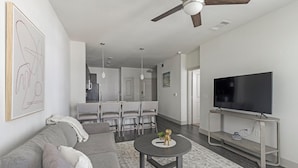 A modern living room with a grey sofa, a coffee table, a flat-screen TV on a stand, and a ceiling fan.