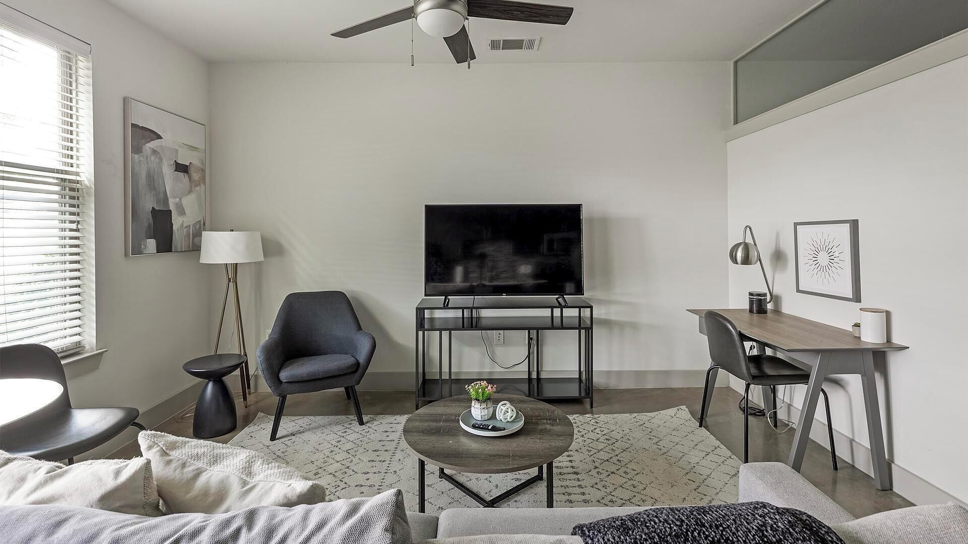Un soggiorno moderno con televisione a schermo piatto, ventilatore a soffitto, zona pranzo con tavolo e sedie in legno, e un'accogliente area relax con divano e poltrone.