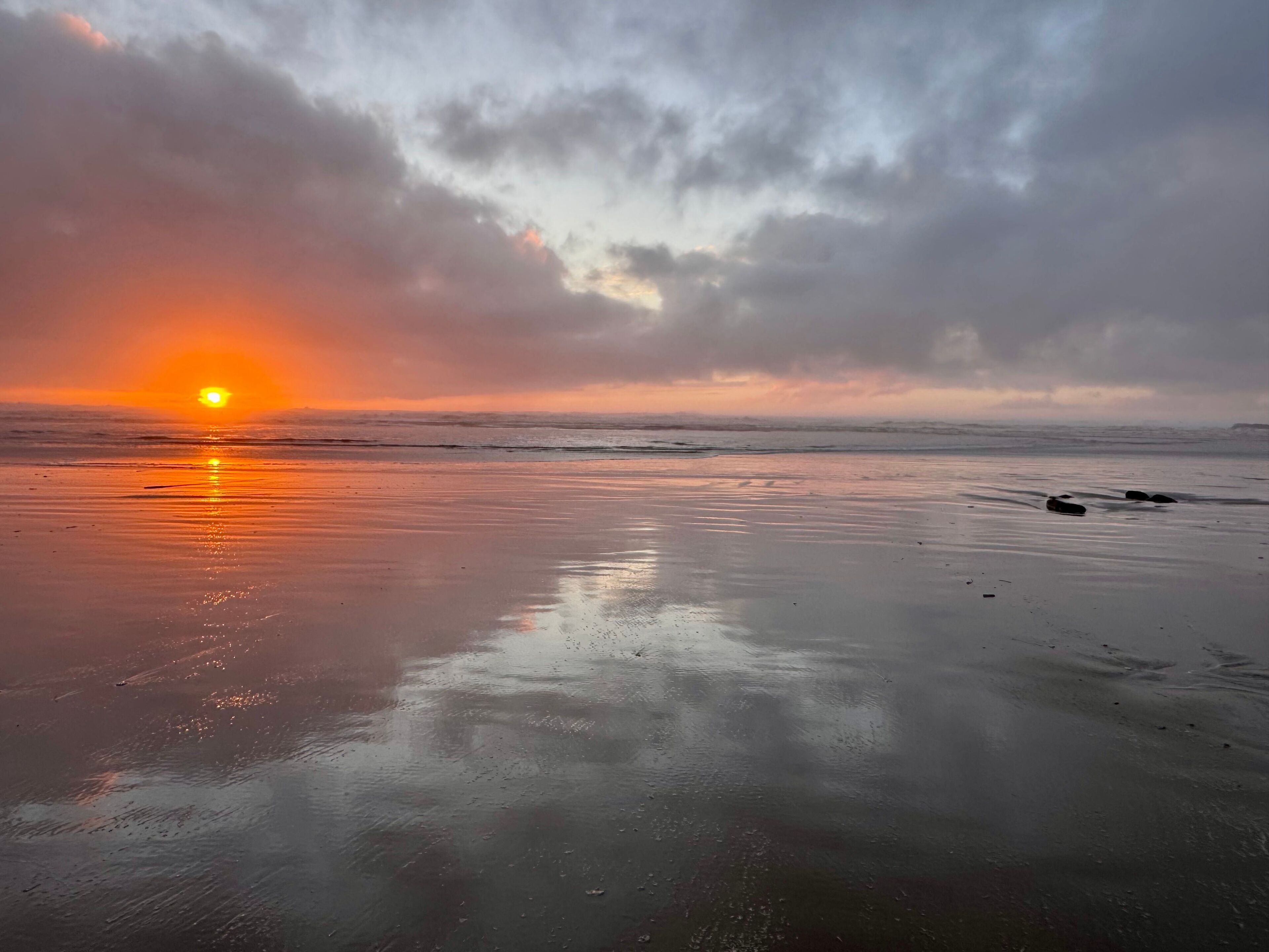 Una playa con atardecer, agua tranquila y cielo nublado.