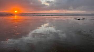 Una playa con atardecer, agua tranquila y cielo nublado.