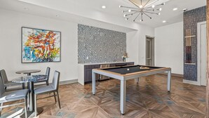 A modern room with a pool table, a dining area with chairs, and a colorful abstract painting.