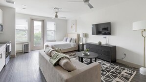 A modern hotel room with a bed, sofa, dining area, and TV.