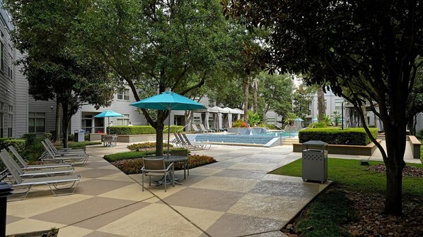 A courtyard with a pool, lounge chairs, and umbrellas.