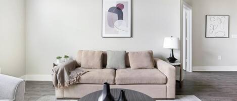 Una sala de estar con un sofá color beige, dos jarrones sobre una mesa redonda y arte abstracto en las paredes.