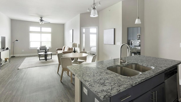 A modern kitchen with granite countertops, a stainless steel sink, and a dining area with a round table and chairs.