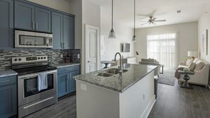 A modern kitchen with blue cabinets, stainless steel appliances, and a granite countertop. - Landing | Stylish 1BD, Pool, Gym (League City)
