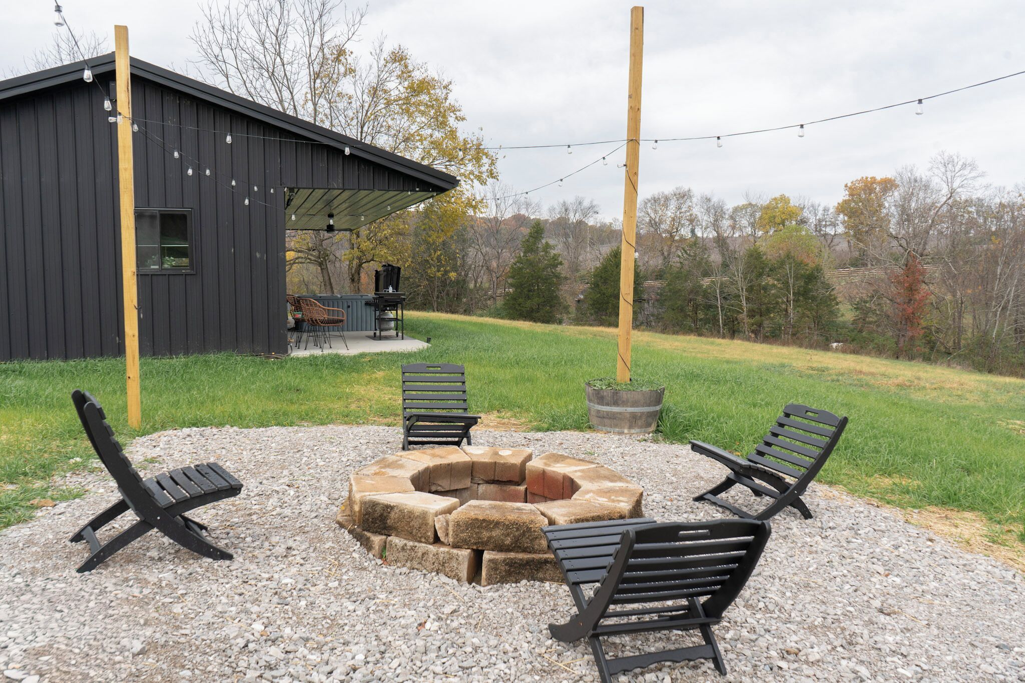 A covered outdoor seating area with a fire pit, surrounded by benches and a rustic building in the background.