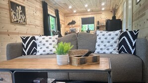 A cozy cabin interior with a sofa, a coffee table, and a bookshelf. - The Barrel Proof Bourbon Trail Cottage Private Hot Tub Firepit Lawrenceburg Ky. (Lawrenceburg)