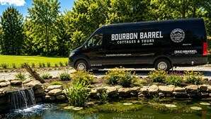 A black van parked by a pond with a waterfall, surrounded by greenery and flowers. - The Barrel Proof Bourbon Trail Cottage Private Hot Tub Firepit Lawrenceburg Ky. (Lawrenceburg)
