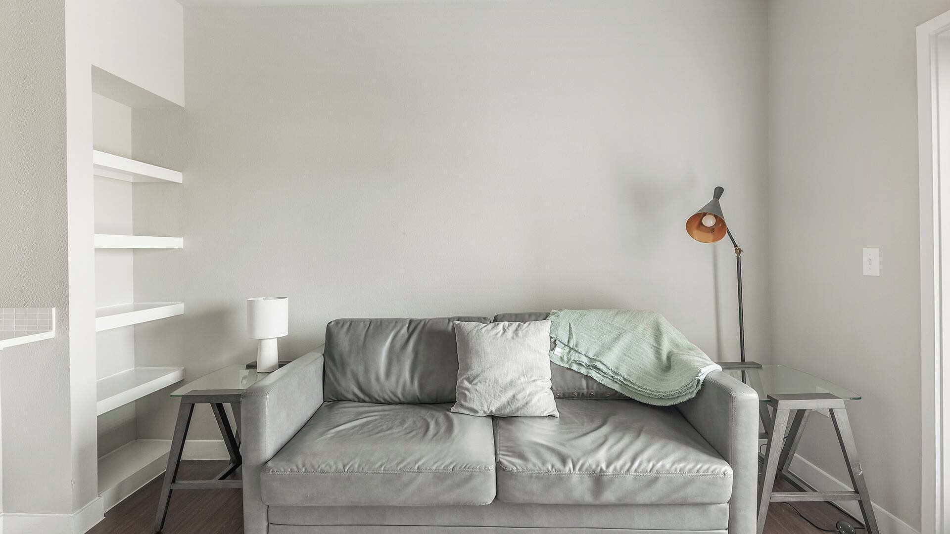 En minimalistisk stue med en grå lædersofa, en hvid lampe og en gulvlampe.